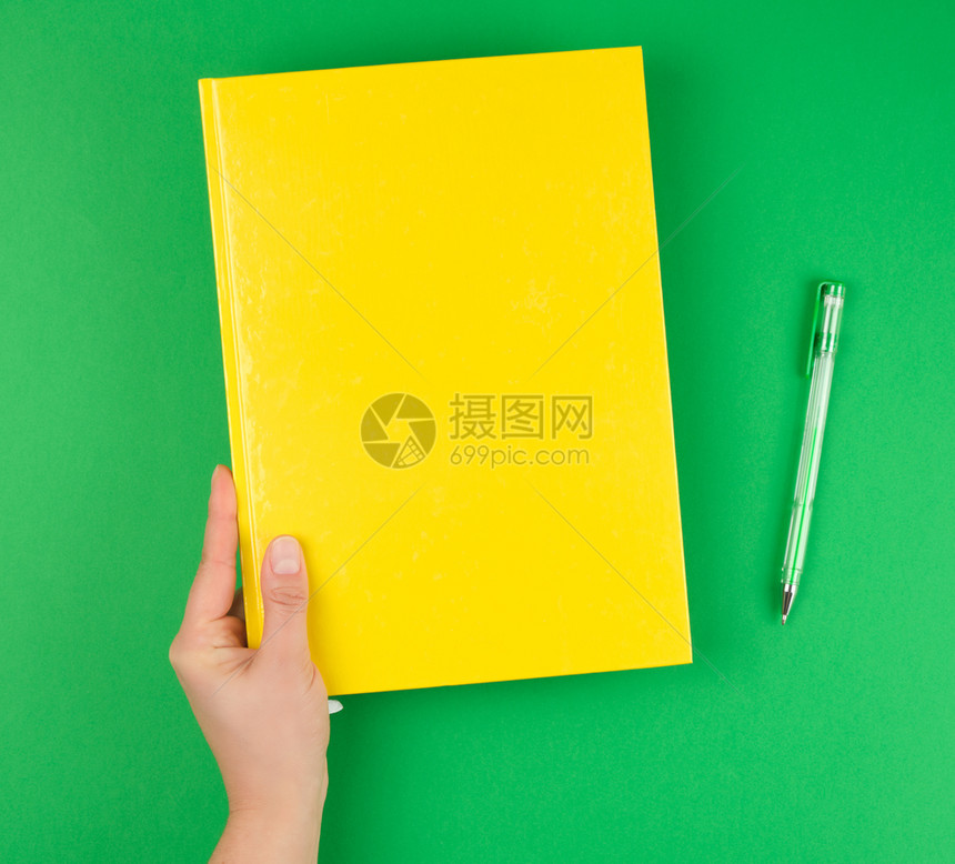 女手握黄色封闭笔记本和绿色背景顶视图图片