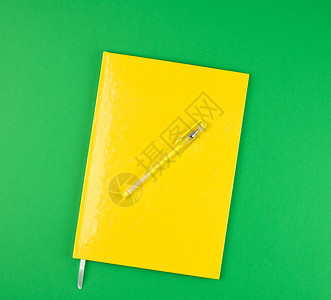 绿色背景顶视图上的黄色关闭笔记本和黄色图片