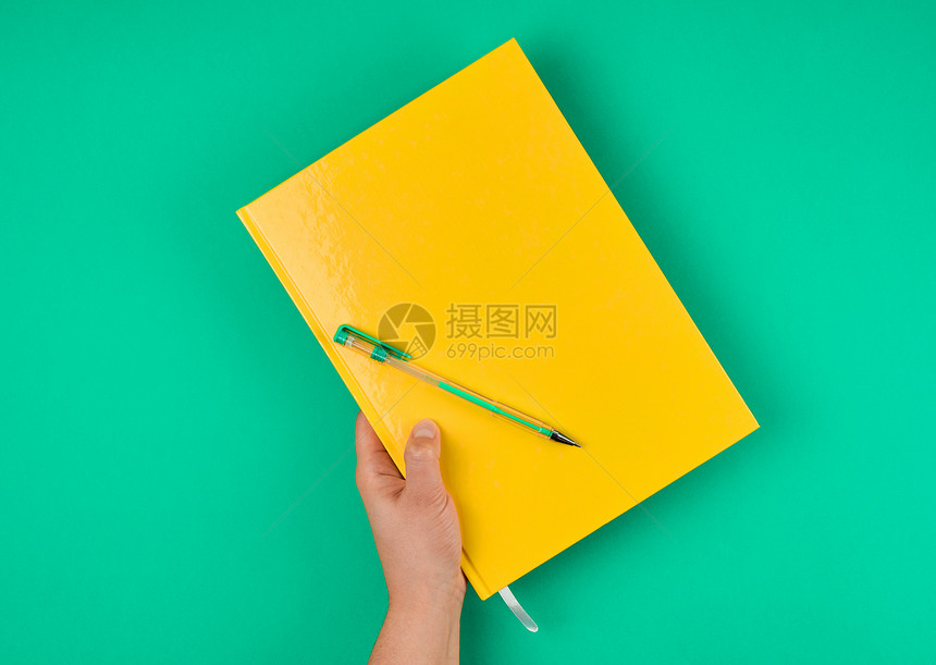 手握大型封闭的黄色笔记本和绿顶视图图片