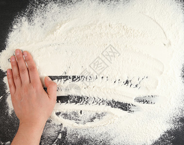 散布在黑色背景和女手上的白面粉厨房背景顶视图图片