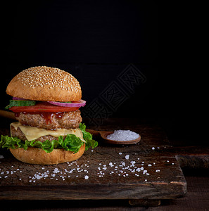 带芝麻种子的包中芝士汉堡间新鲜蔬菜和肉串黑色背景图片