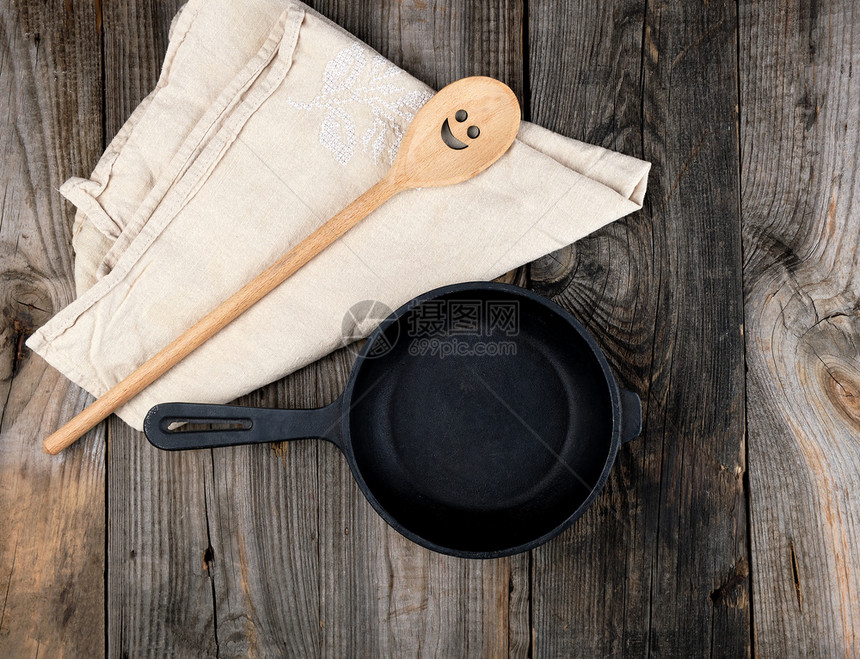 顶视图在木制桌子上用把手和木勺的黑圆煎锅图片