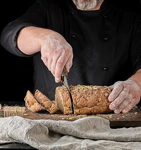 面包师把刀切成黑麦面包底棕色木板上的南瓜种子图片