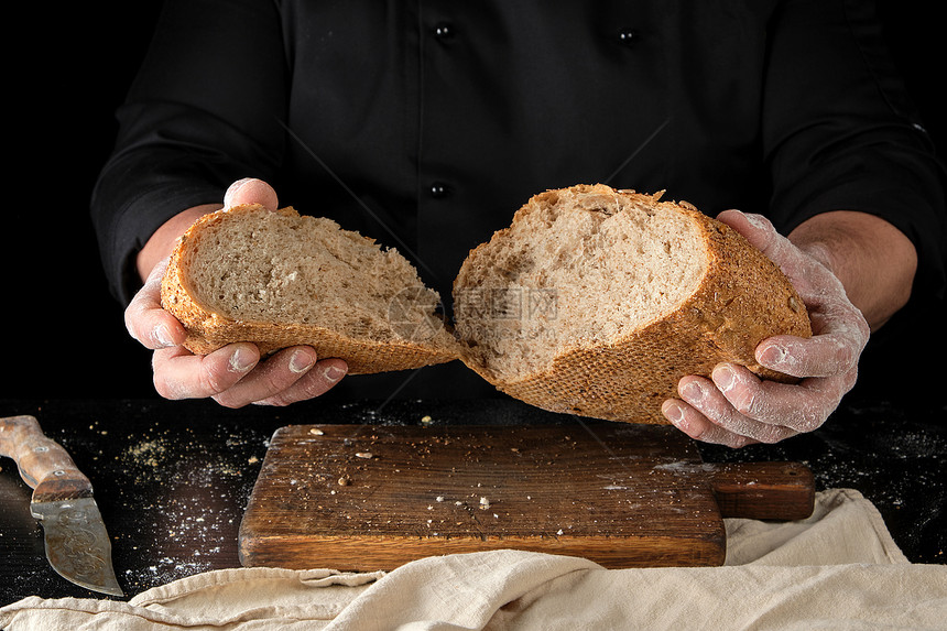 身穿黑色制服的厨师坐在桌边半圆黑麦面包中折断图片