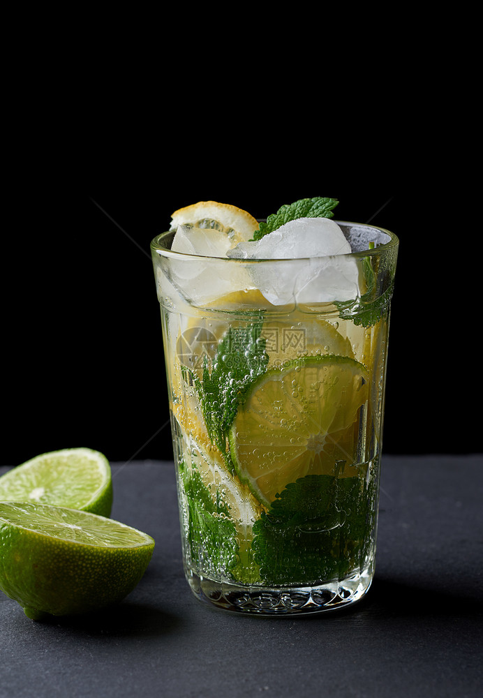 用新鲜柠檬石灰绿色薄荷和黑底玻璃杯中的冰块制成冷柠檬图片