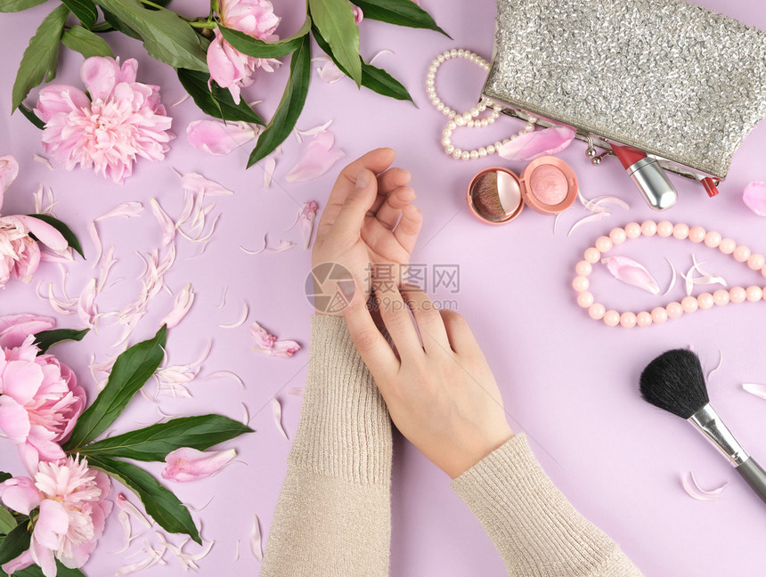两只手皮光滑的年轻女孩手袋有化妆品花朵盛开的粉红条时尚的概念顶级风景图片
