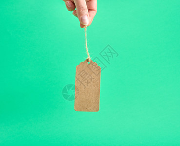 绿色背景的绳子上挂着纸面棕色空白标签的女手图片