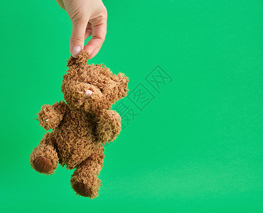 雌手握着一只小泰迪熊在绿背景的耳朵边复制空间图片