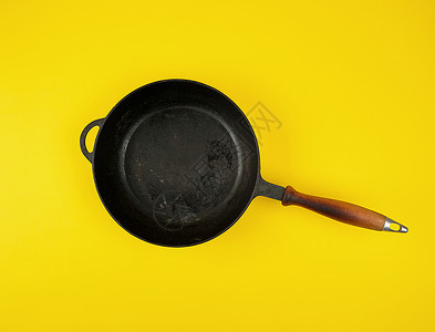 黑色圆铁环煎锅黄背景的木柄平面图片