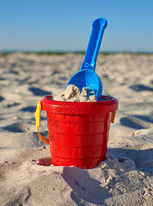 红色铲子玩具在海滨夏日旅行和节假的背景带沙子和铲的红色婴儿塑料桶红色婴儿塑料桶沙子和铲背景