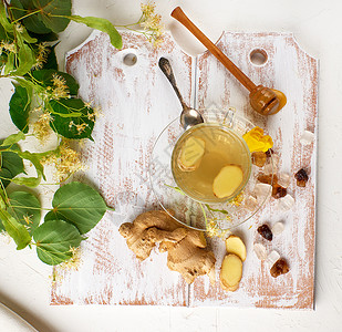 茶杯透明来自姜和叶子在白木板上旁边的糖块和树枝绿色的叶子图片