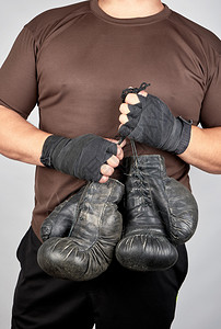 穿着棕色衣服的运动员带着非常古老的皮革黑色拳击手套白底图片