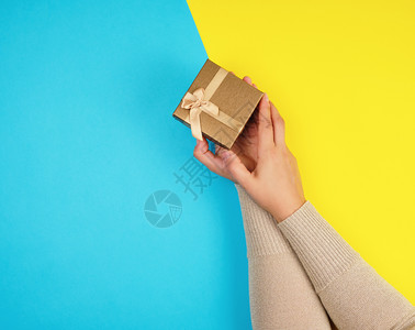 妇女手握着一个封闭的盒子在蓝黄背景顶视图复制空间上鞠躬图片