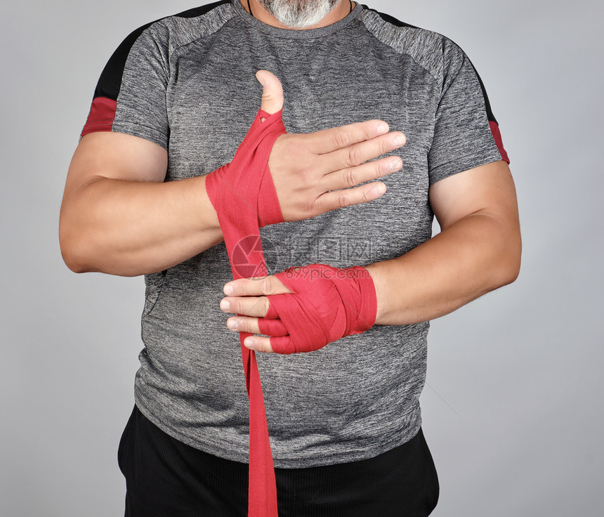运动员穿着灰色衣服站立在训练前用红色纺织弹绷带包住手灰色背景图片