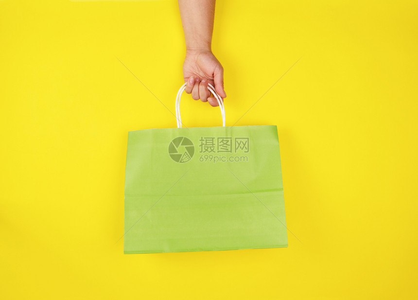 持有黄色背景季节销售概念绿纸袋的女手持绿纸袋图片