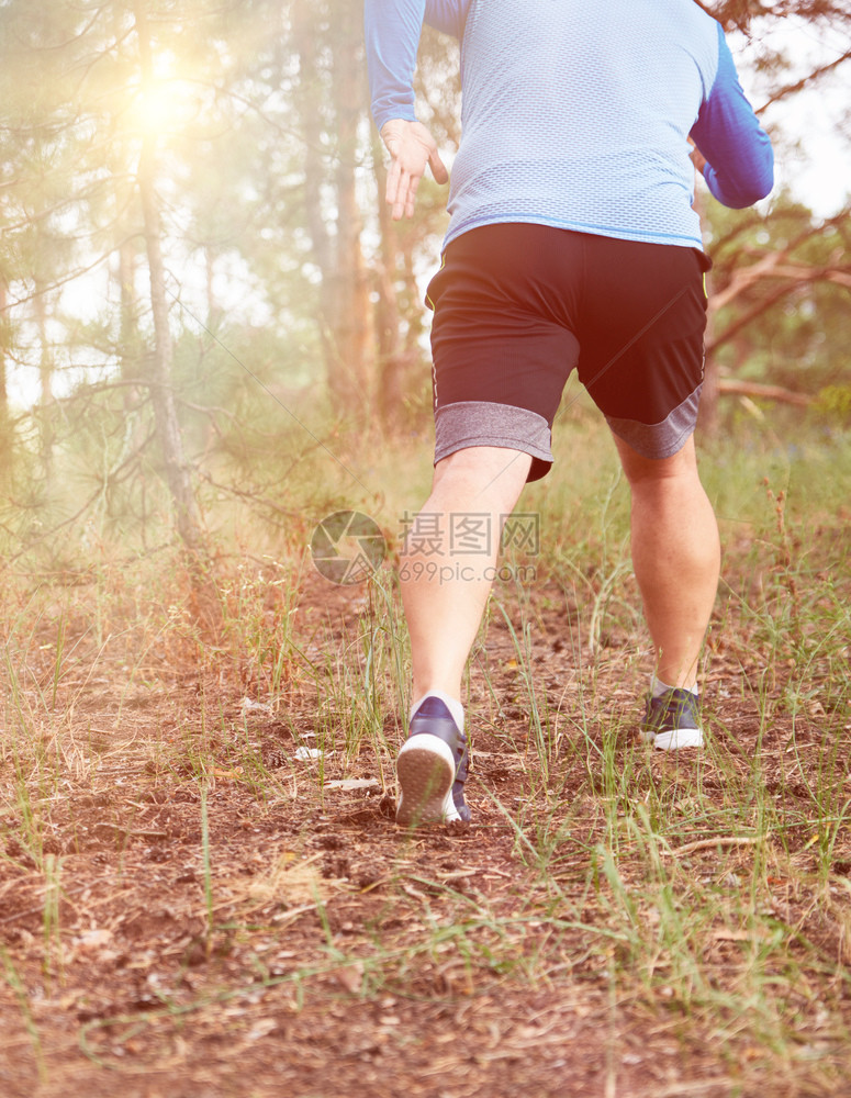 身穿蓝衣服和黑短裤的成年男子在阴险的森林中奔跑对抗明亮的太阳健康生活方式的概念和在新鲜空气中奔跑图片