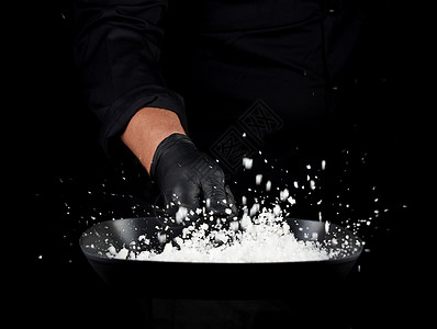 身穿黑色制服的主厨拿着一个有白盐的锅子吐出有选择焦点模糊调味粒子图片