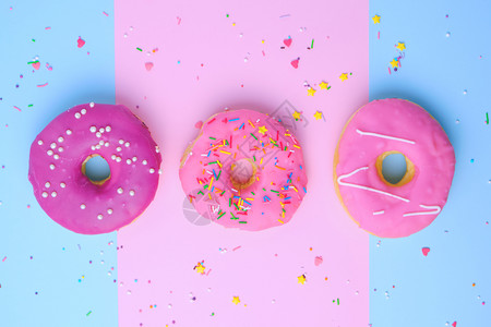 三个圆形甜圈喷洒在粉红蓝背景上糊面颜色顶视图上图片