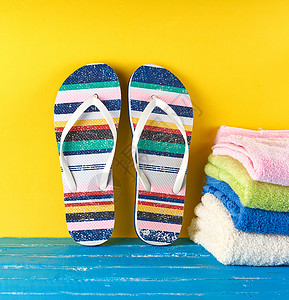 两对女海滩拖鞋和蓝黄色背景的毛巾海上度假的概念图片