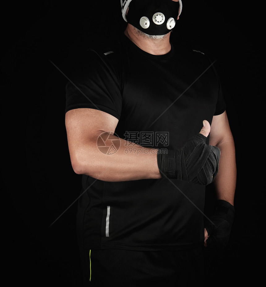 身穿黑色制服的运动员训练蒙面和双手用黑色绷带站着显示手势如黑色背景图片