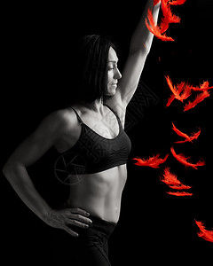 身穿黑胸罩运动的年轻美女将红羽毛扔在黑暗背景上模特站在侧面图片