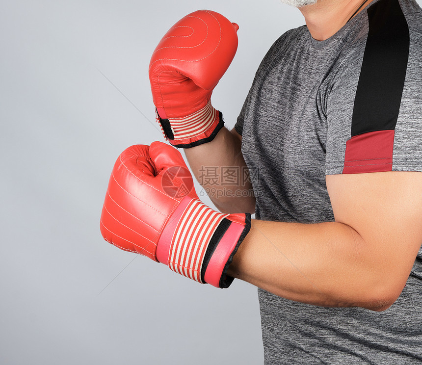 身穿灰制服和红皮拳击手套的成年男子运动员身穿灰色制服和红皮拳击手套站在白背的架子上图片