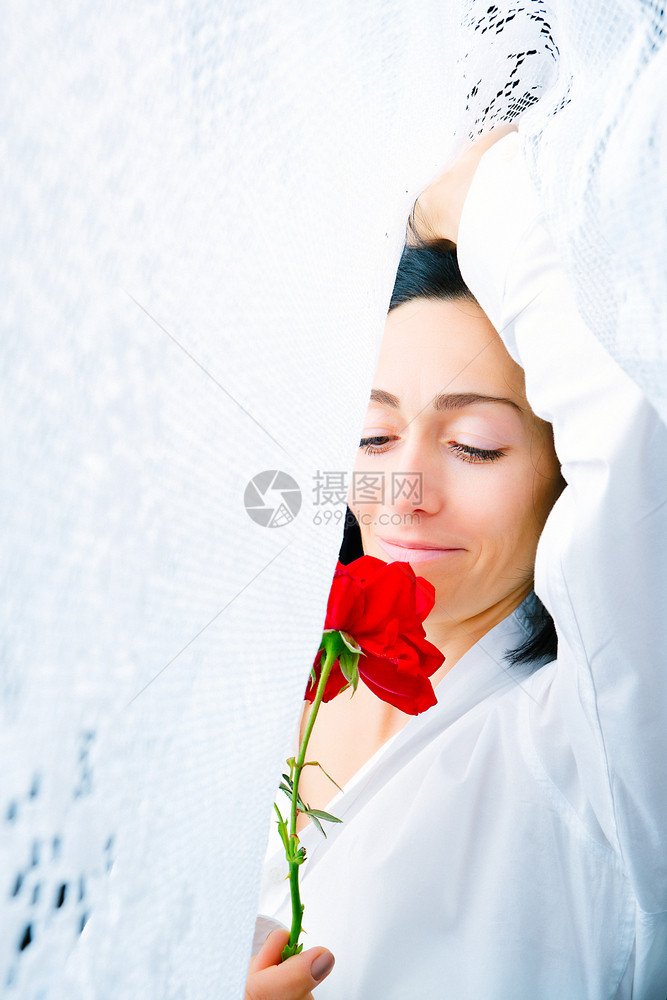 一位年轻女子的肖像她手上拿着一朵红玫瑰手被白窗帘环绕紧环绕清晨醒来图片