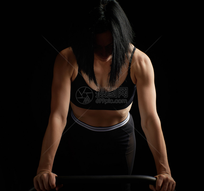 身穿黑胸罩肌肉的年轻运动女青怀着双臂在健身和运动中弹着低键摄影棚图片