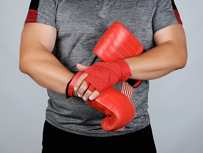 身着蓝衣服的运动员手被红色的纺织绷带连着他穿皮运动拳击手套灰色背景背景图片