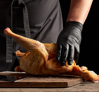 黑乳胶手套主厨在棕色切面板上 拿着一整具鸡肉 类烹饪过程黑暗背景背景图片