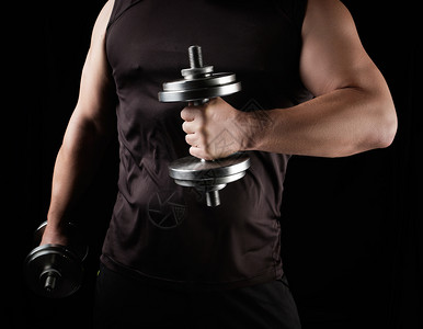 穿黑衣服的男人手里握着钢铁哑铃他的肌肉很紧张低键运动背景图片