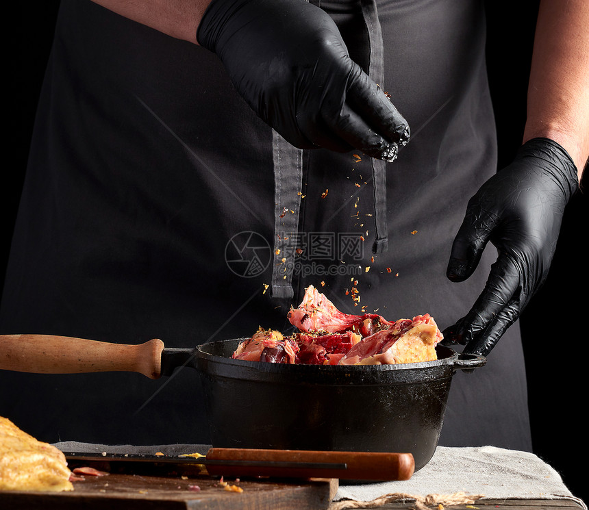 穿黑色制服和乳胶手套的厨师用黑色铸铁的铲子和烹饪用生鸡肉做鲜图片