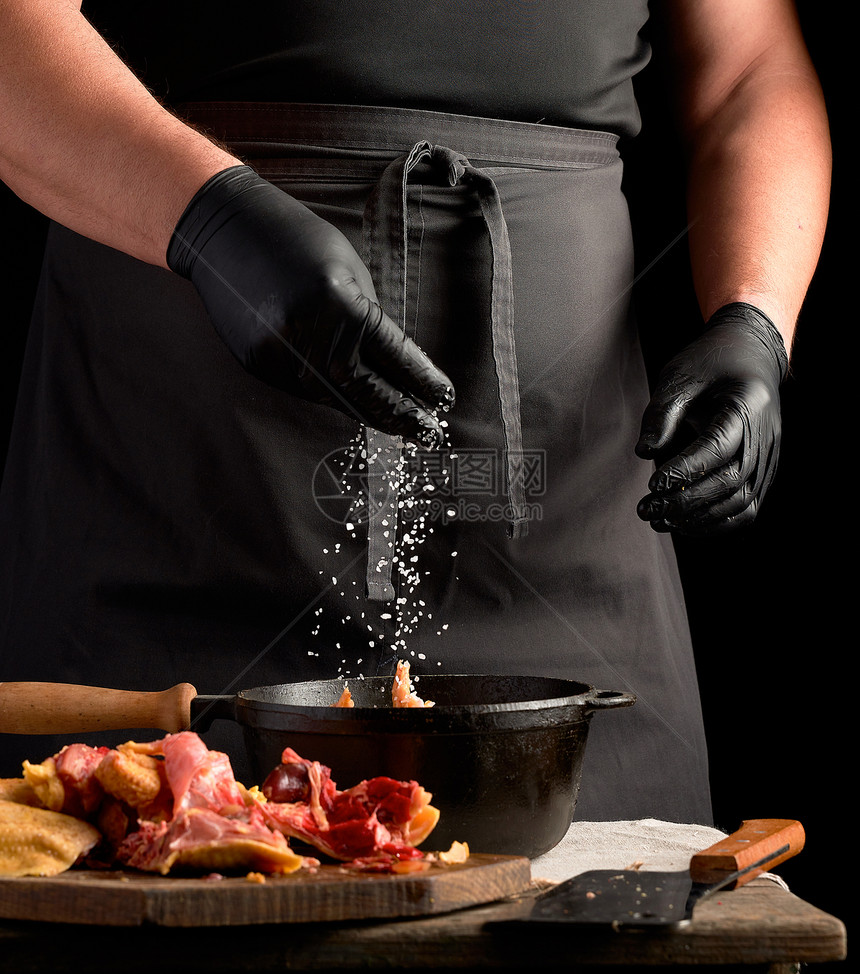 黑制服主厨和穿色制服的乳胶手套喷洒着白盐生鸡肉在黑铁煎锅里烤鸡肉做饭图片