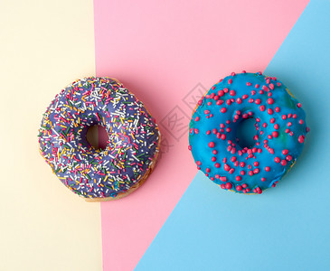 圆面包甜圈有彩糖喷洒蓝在粉红色黄背景上加蓝甘糖霜最高视图图片