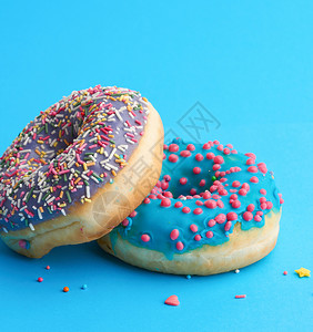 两圆面包甜圈配有彩糖喷洒和蓝彩染底背景图片