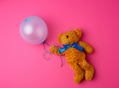 棕色小泰迪熊拿着蓝色膨胀的气球在粉红背景的绳子上图片