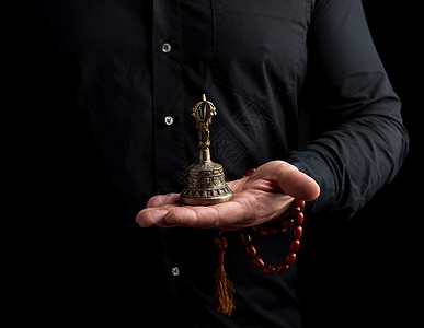 身穿黑衬衫的成年男子拿着铜藏仪式钟图片