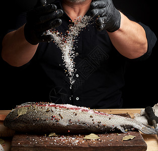 黑衬衫主厨和乳胶手套准备木制切板上的鲑鱼片配香料和盐低键图片