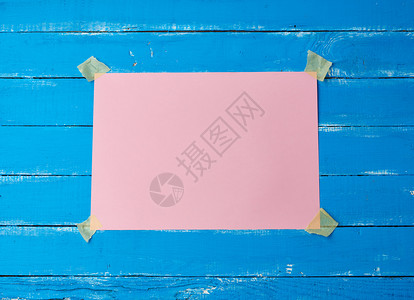 用胶带把一张粉红色的长方形空白纸粘在蓝色的木制背景上作为题词的地方图片