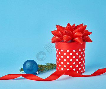 蓝色圆点边框圆形的红色纸板箱白色圆点带蝴蝶结云杉枝蓝色背景上有一个闪亮的蓝色球圣诞节的背景背景