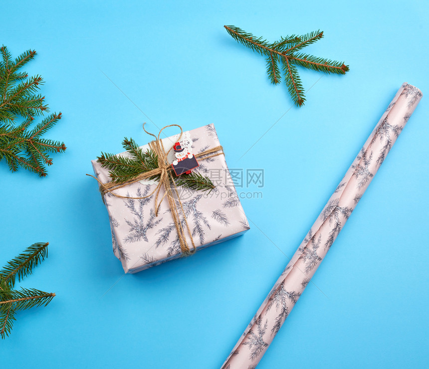包着粉红纸的礼物绑着棕色绳子绿树枝的装饰品蓝色背景顶层风图片