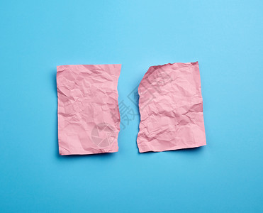 粉红色纸片被撕成两半在蓝色背景上被撕碎纸片的边缘图片