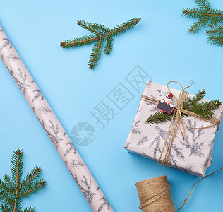 包着粉红纸的礼物绑着棕色绳子绿树枝的装饰品蓝色背景顶层风图片