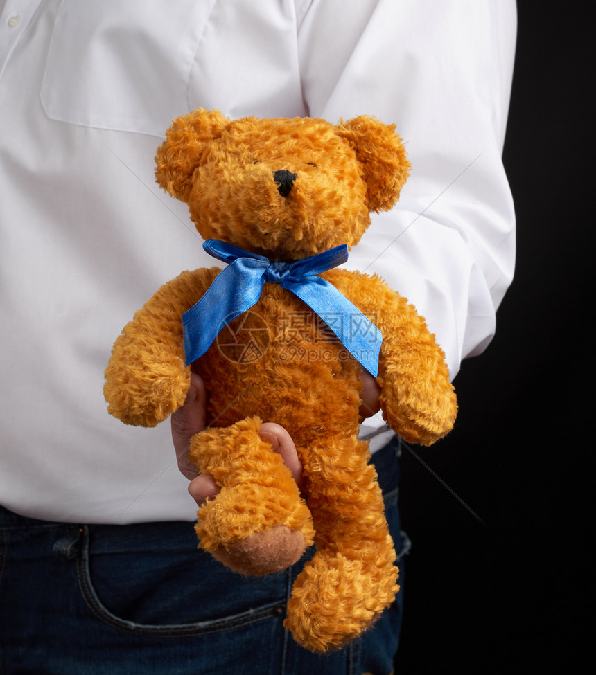 穿白衬衫的成年男子在黑暗背景上带着棕色的泰迪熊关上图片