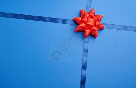 蓝丝带在红弓中间的深蓝色背景上穿透仿佛绑着礼物顶视线图片