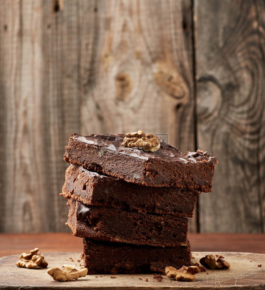 一堆正方形烤焦巧克力蛋糕片和木质表面的胡桃自制食品巧克力糕点甜食自制点木餐桌图片