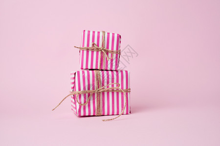 两盒用粉红纸包着的两盒用棕色绳子绑在粉红背景假日上图片