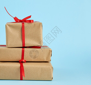 包裹在棕纸上并用红弓捆绑的一堆箱子蓝色背景的礼品复制空间图片