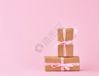 包装在着棕色Kraft纸和粉红色背景上带有粉红色丝的盒装礼物图片