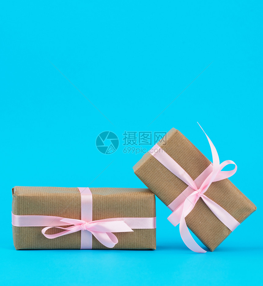 包在着棕色Kraft纸的盒装礼物中并用蓝色背景的粉丝带绑在蓝背景上图片